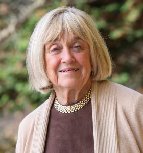 Woman with blonde bob haircut and beige cardigan smiles at the camera